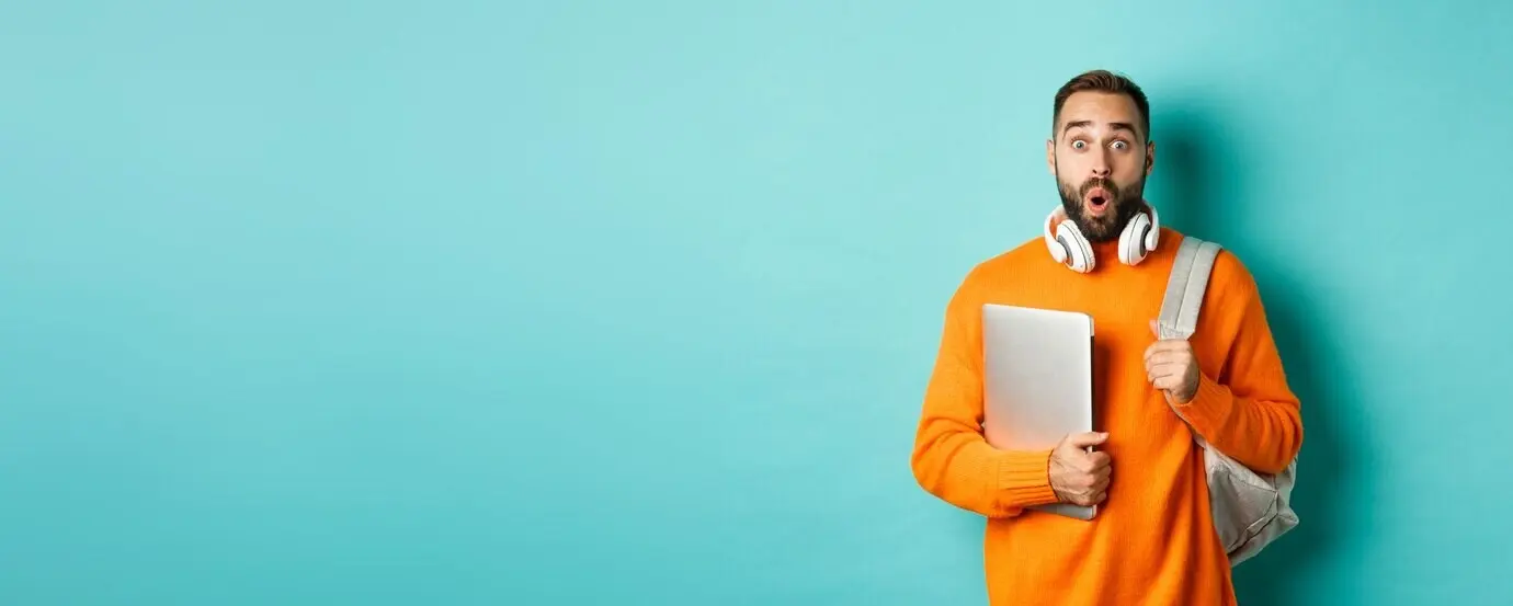 Ein fröhlicher Mann mit Rucksack und Kopfhörern hält einen Laptop, lächelt überrascht und steht über tu.